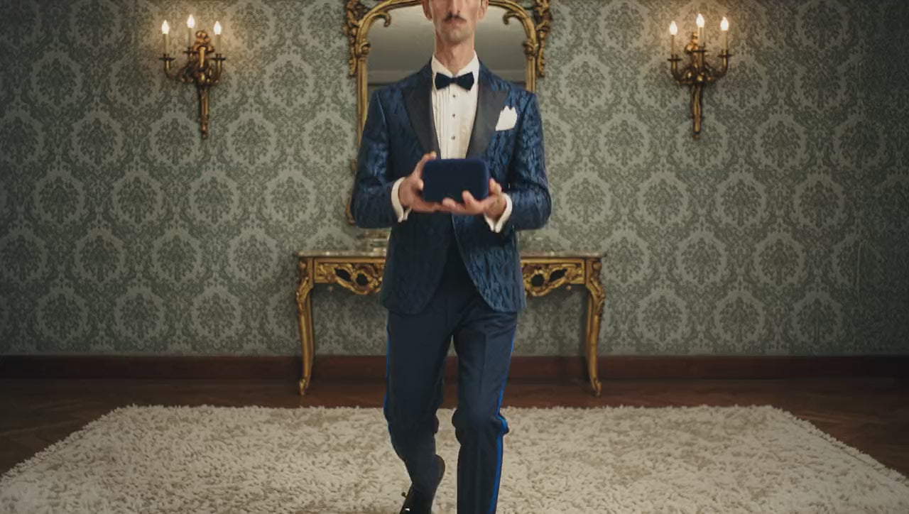 The butler kneels and opens a ring box holding a pack of butter